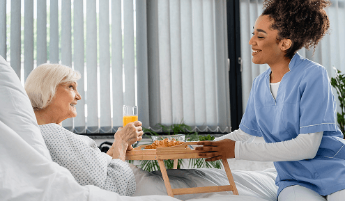 A carer bringing breakfast to a client resting in bed