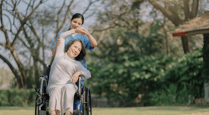 A support worker walking beside a smiling client in a wheelchair outdoors